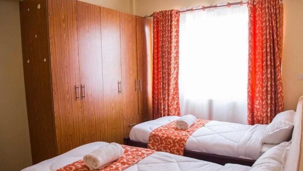 Habitación de hotel con dos camas, un armario y cortinas rojas estampadas.