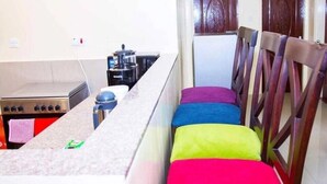 Una cocina con estufa, cafetera y sillas con cojines de colores.
