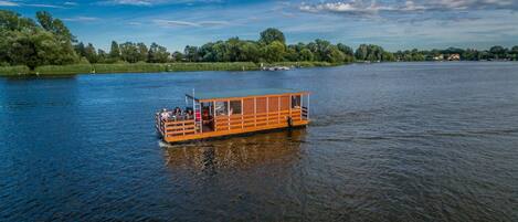 A wooden boat with a covered deck and seating area, floating on a calm river.