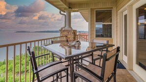 A covered outdoor patio with a glass table and chairs, overlooking a body of water and greenery. - Branson Lakefront Penthouse at The View- Emerald Pointe! (Hollister)