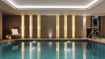 Una piscina con vista despejada al agua, una silla de descanso y una pared con lámparas verticales.