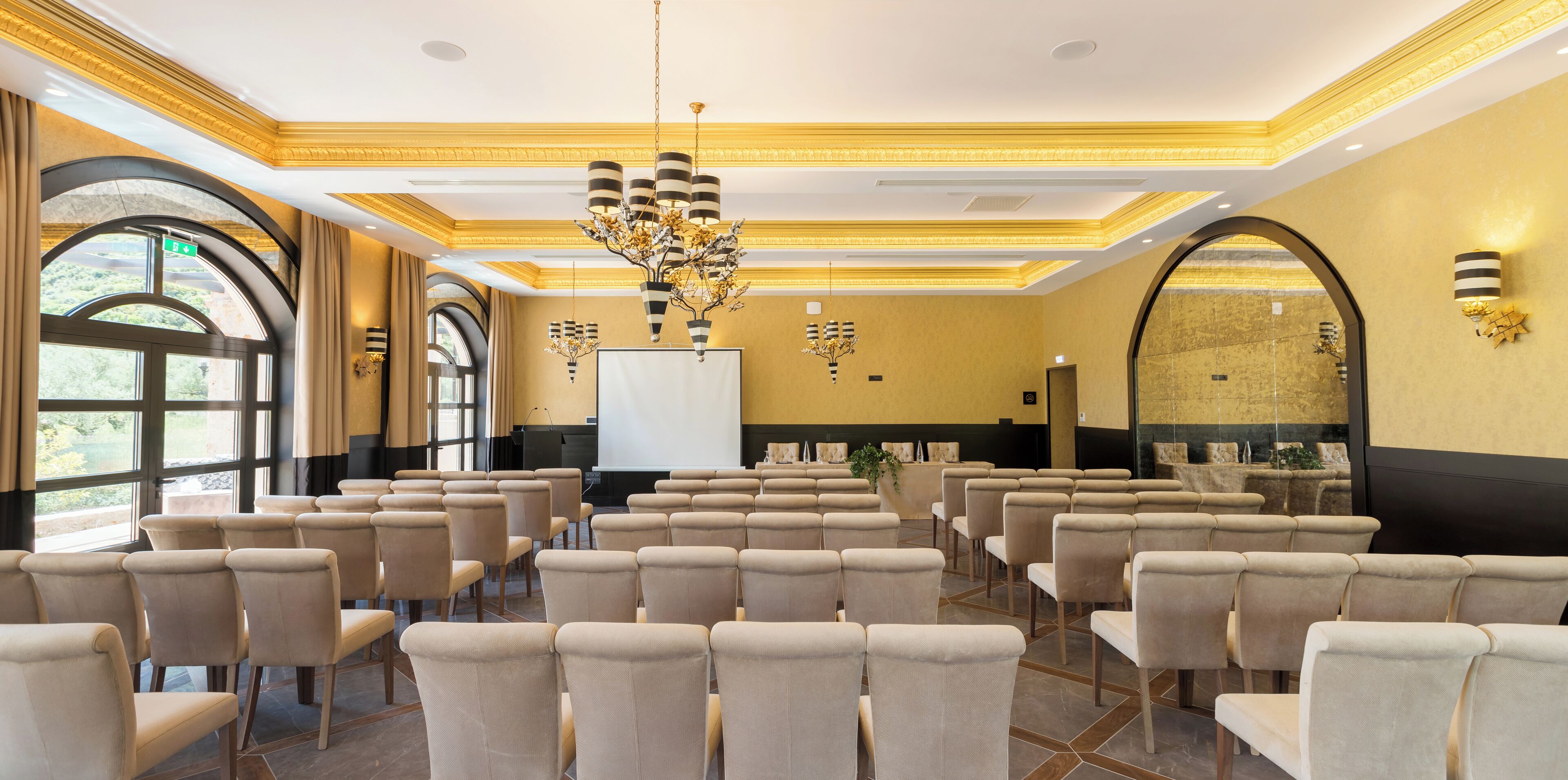 A conference room with rows of chairs, a projector screen, and a large chandelier.