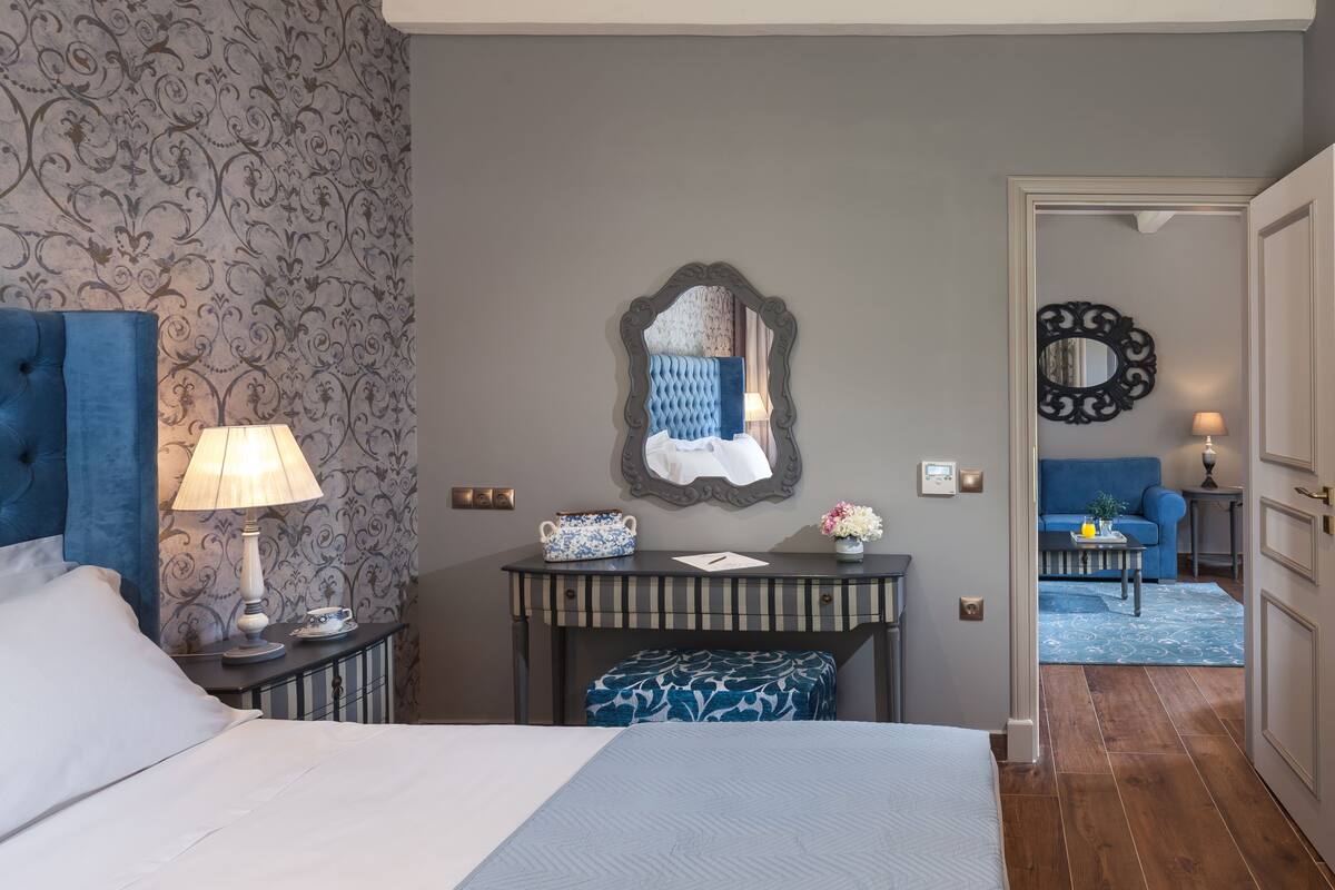 A hotel room with a large bed, a nightstand, a dresser, a mirror, and a seating area with a blue sofa and a small table.