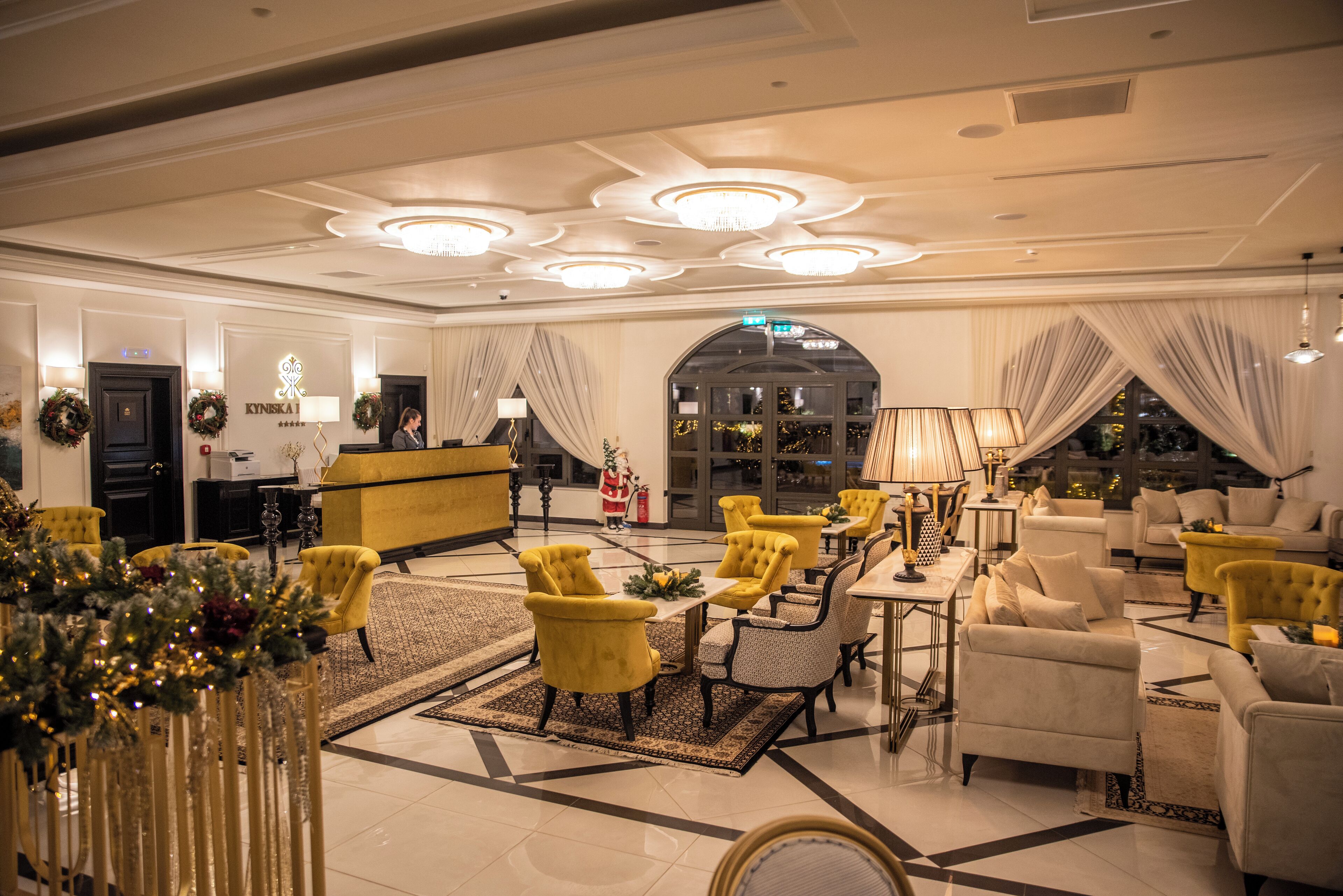 Un hall de hotel con sillones amarillos, un mostrador de recepción y una gran lámpara de araña.