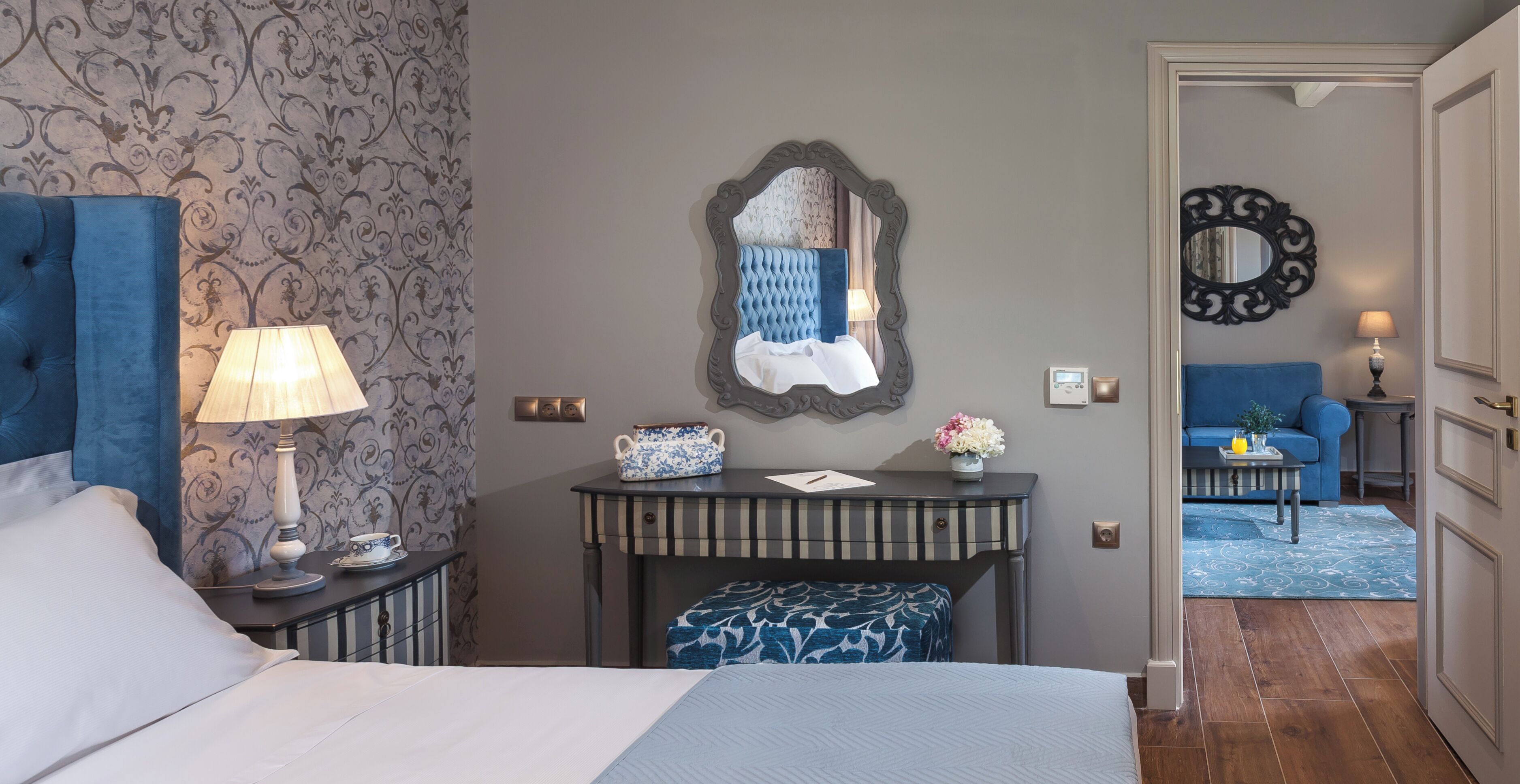 A hotel room with a bed, bedside tables, a dresser, a mirror, and a view of the hallway.