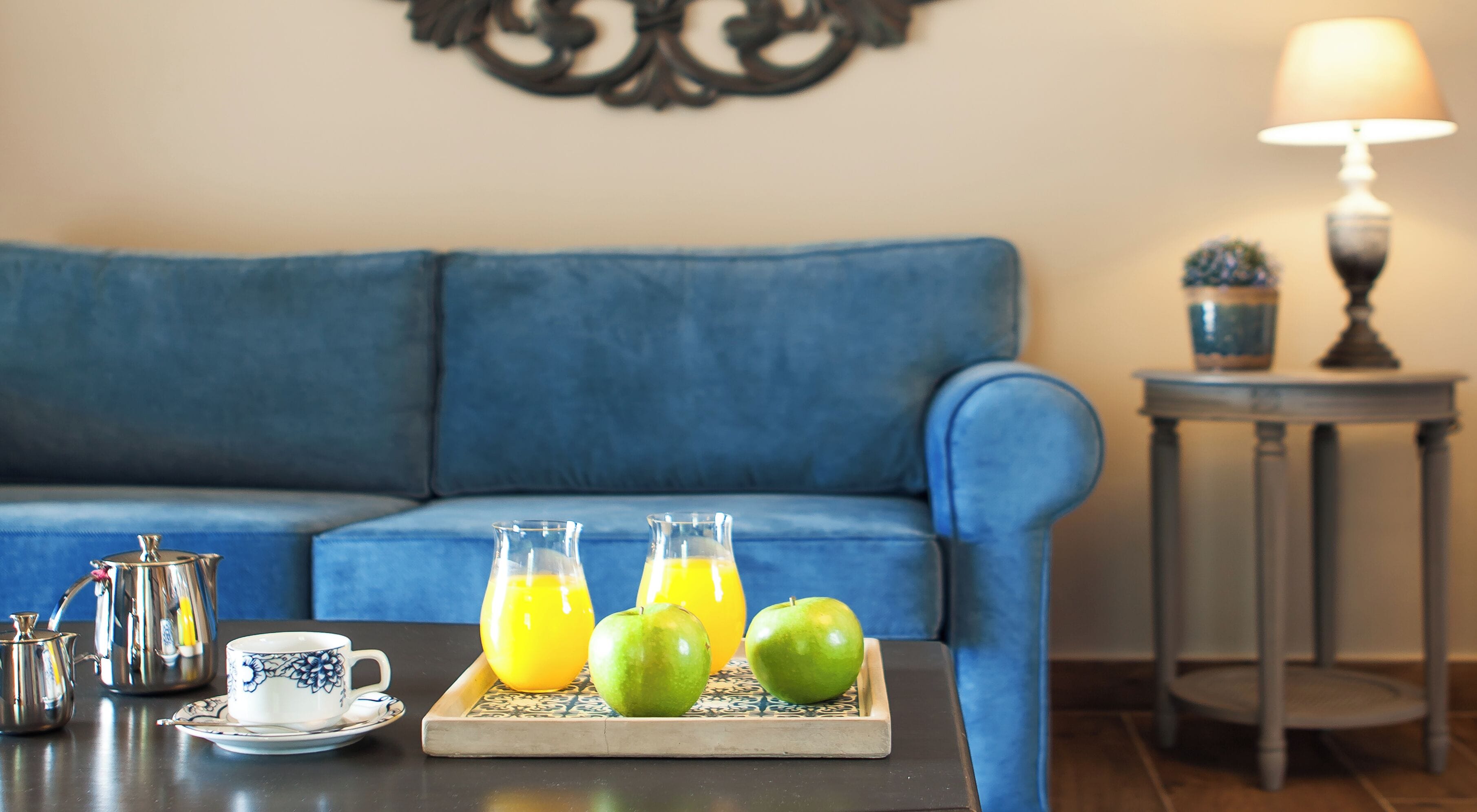 Un salón con un sofá azul, una mesa de centro con una bandeja que contiene una taza, una tetera y dos manzanas.