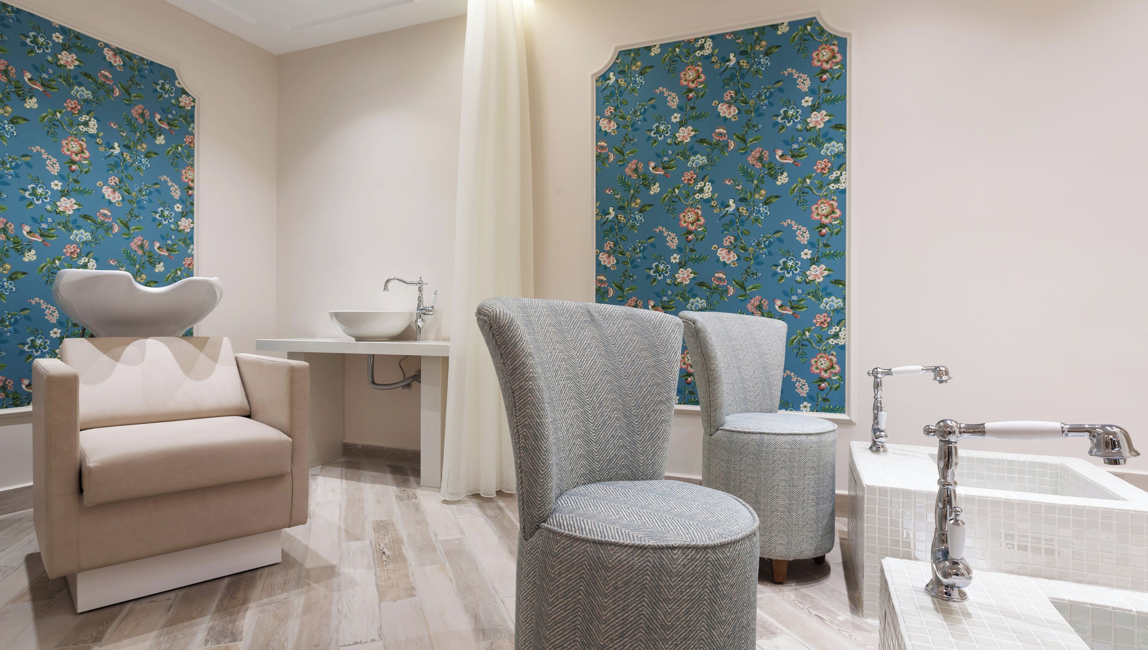 Un baño con lavamanos, dos sillas, bañera y papel tapiz floral.