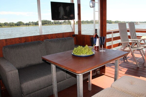 Una terraza con un sofá, una mesa con un bol de uvas y una botella, y una pantalla de televisión.