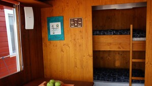 Une chambre avec un lit superposé, un mur en bois, une table avec un panier de pommes et une fenêtre avec des stores.