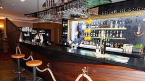 Zona de bar con mostrador de madera, taburetes y una variedad de botellas de licor.