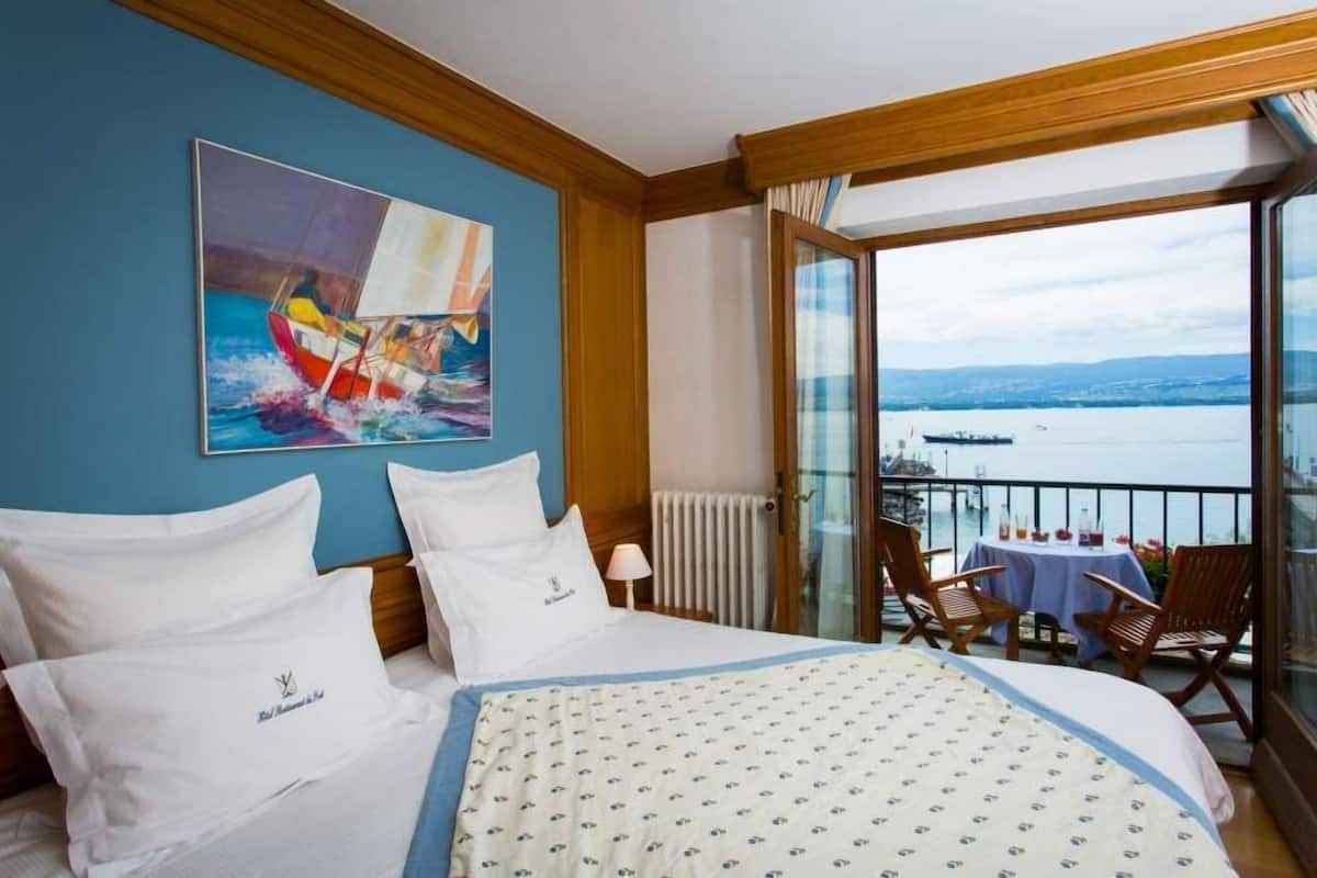 Habitación de hotel con cama, un cuadro de un velero, balcón con mesa y sillas, y vista al mar.