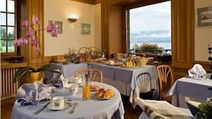 Un comedor con varias mesas dispuestas para el desayuno, mostrando una variedad de alimentos y vistas al exterior.