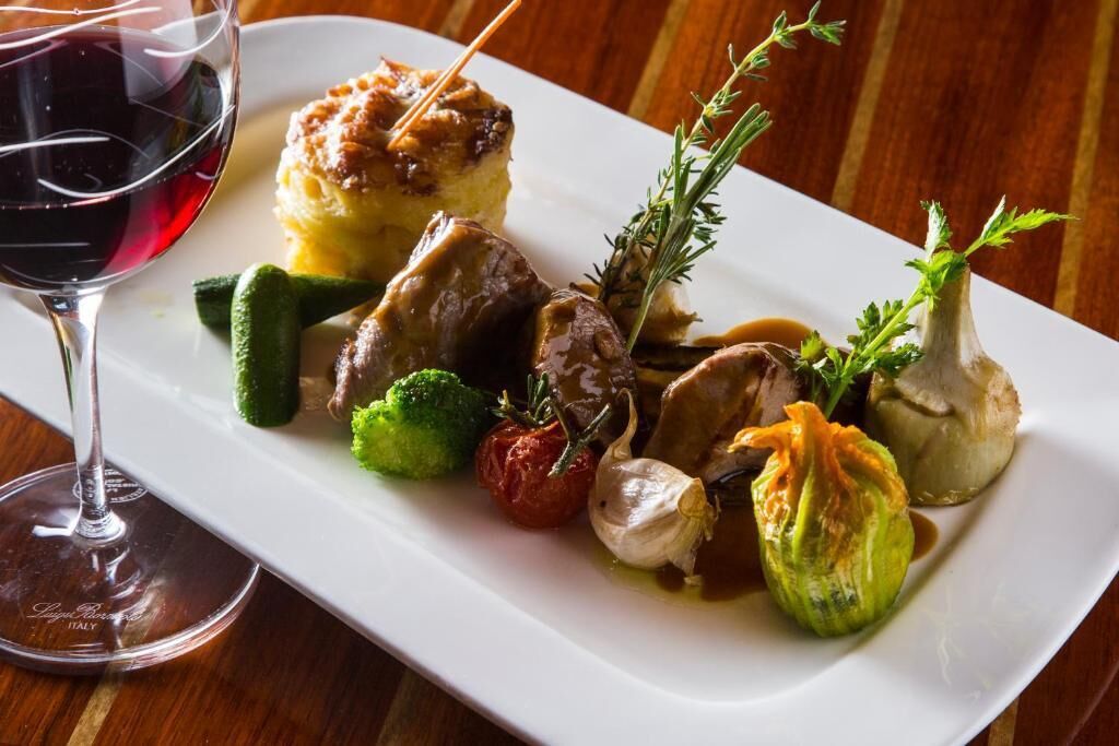 A white rectangular plate with various vegetables and a glass of red wine.