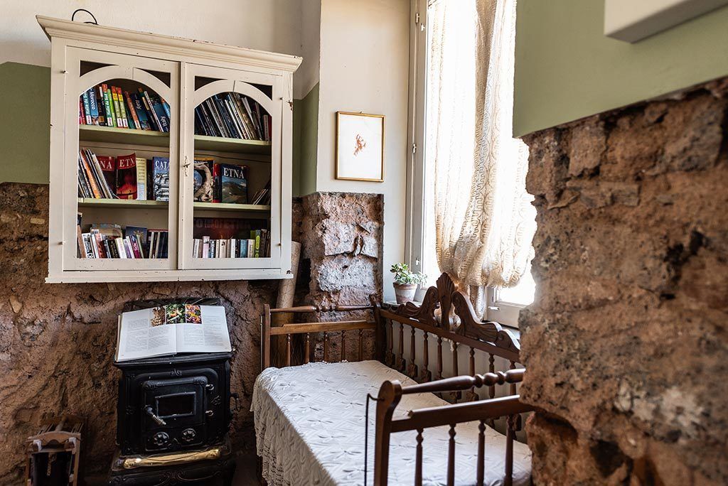 A cozy room with a wooden bed, a white cabinet with books, and a stone wall.