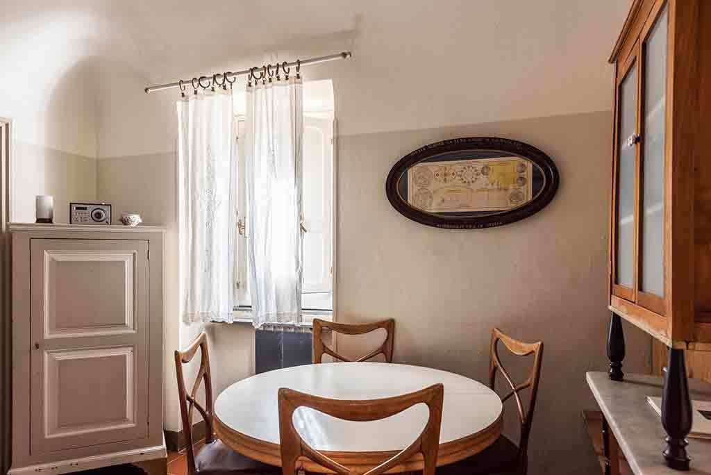 Un coin repas avec une table ronde, quatre chaises en bois, un buffet, une radio et un tableau encadré au mur.