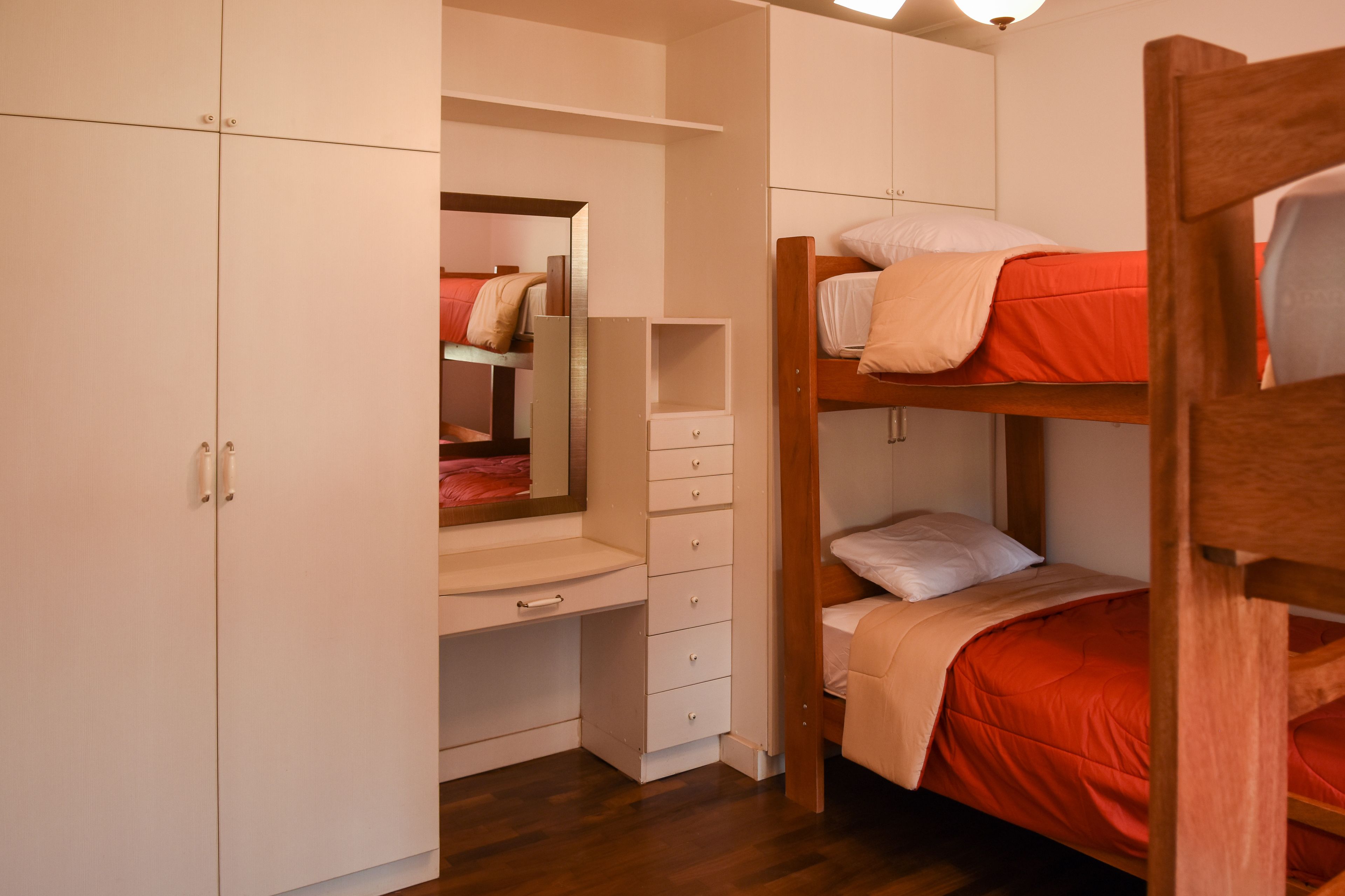 A bunk bed with a red mattress, a wooden desk with drawers, and a white wardrobe.