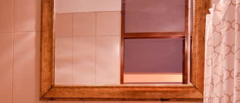 A bathroom with a pedestal sink, a mirror with lights, patterned tiles, and a shower curtain.