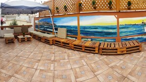 An outdoor seating area with wooden benches and tables, a mural of the ocean, and potted plants. - Lima White House - Hostel (Lima)