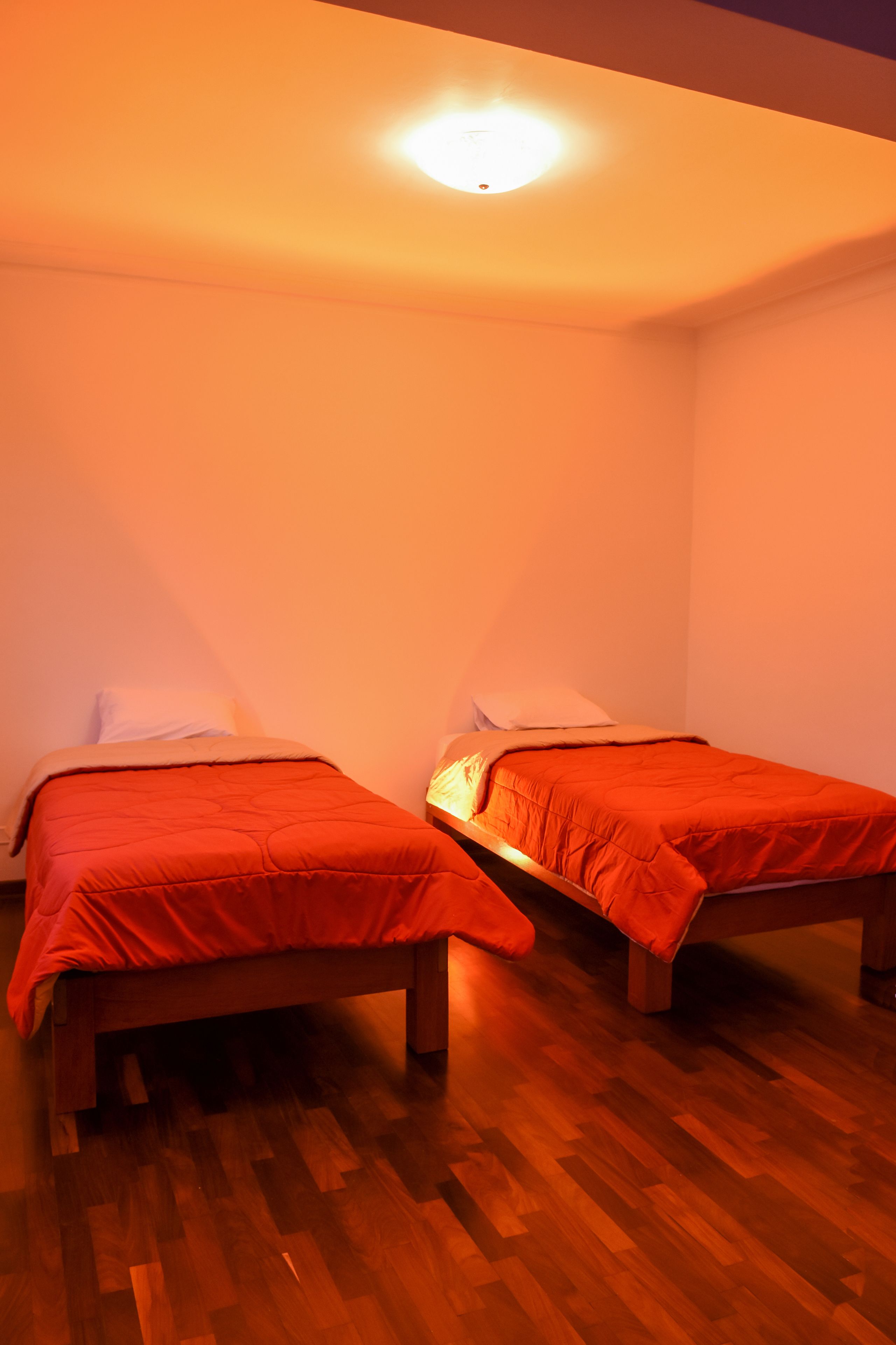 A room with two single beds, wooden flooring, and a ceiling light.