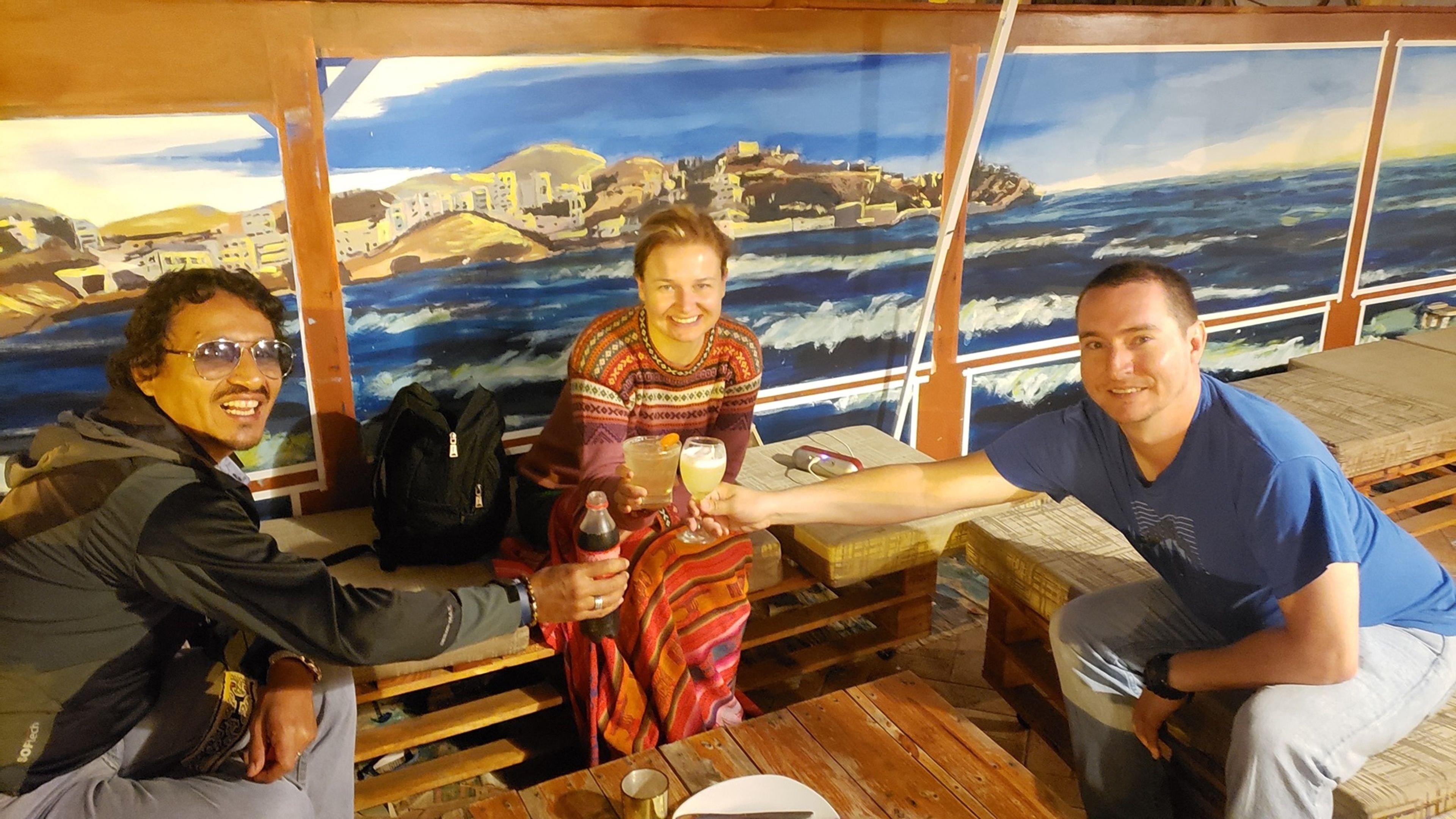 Three people seated at a wooden table with a mural of a coastal scene in the background.