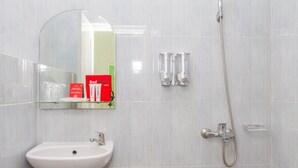 Een badkamer met een witte wastafel, een spiegel, een handdouche en een glazen zeepbakje.