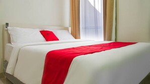 Een hotelkamer met een bed, wit beddengoed, een rood kussen en een raam met gordijnen.
