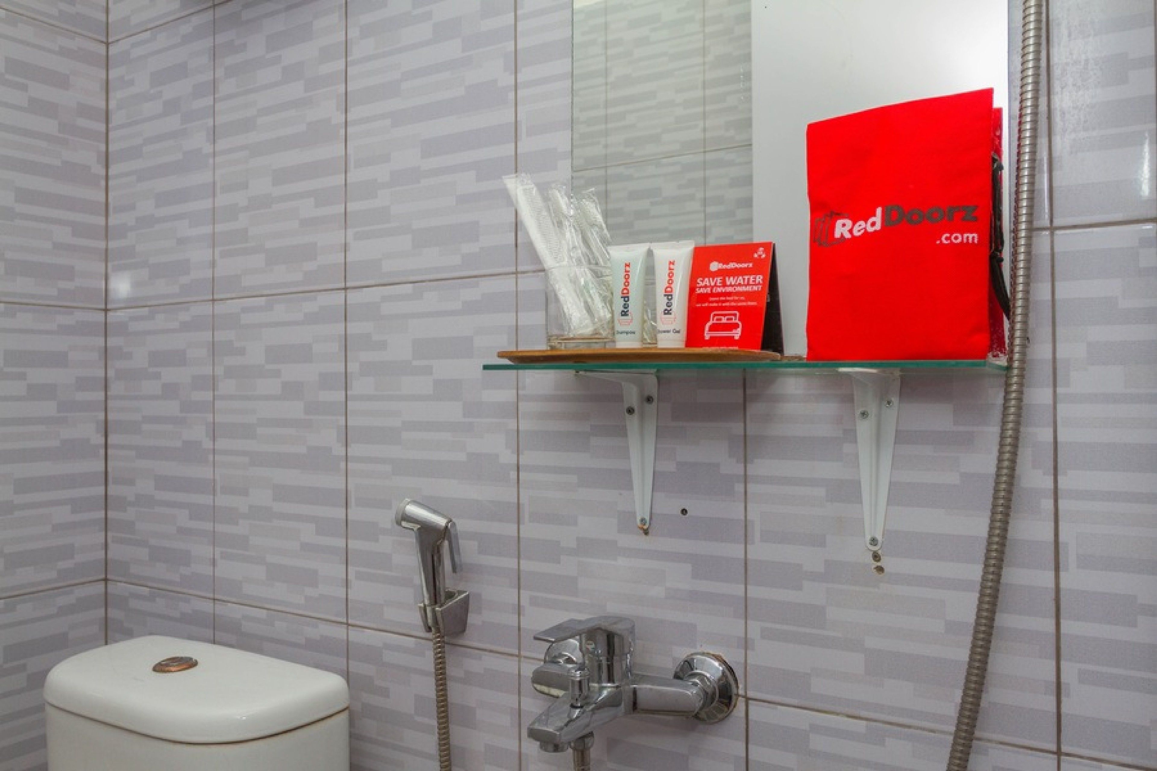 A bathroom with a toilet, a shower, and a glass shelf with RedDoorz products.