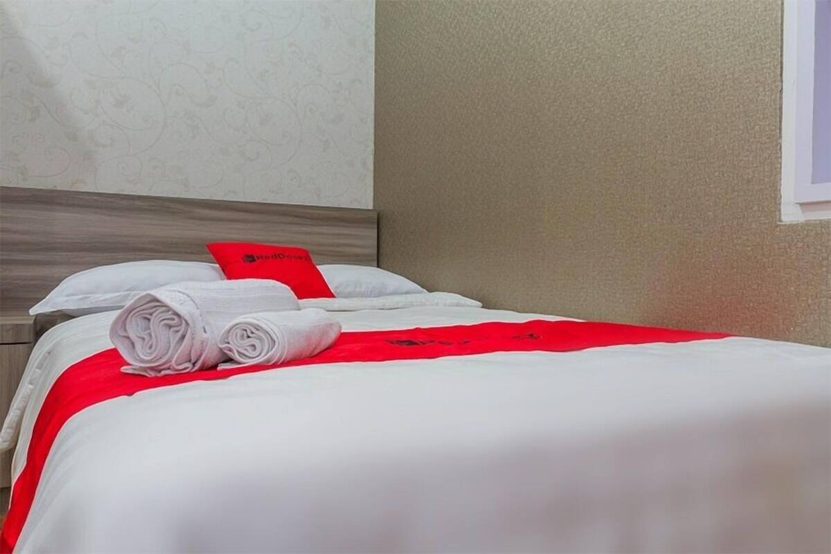 A neatly made bed with a red blanket, white pillows, and a red pillow with a logo.
