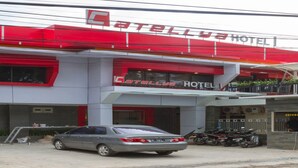Un hôtel à la façade rouge et blanche, avec une voiture garée devant et des motos stationnées à l’extérieur.