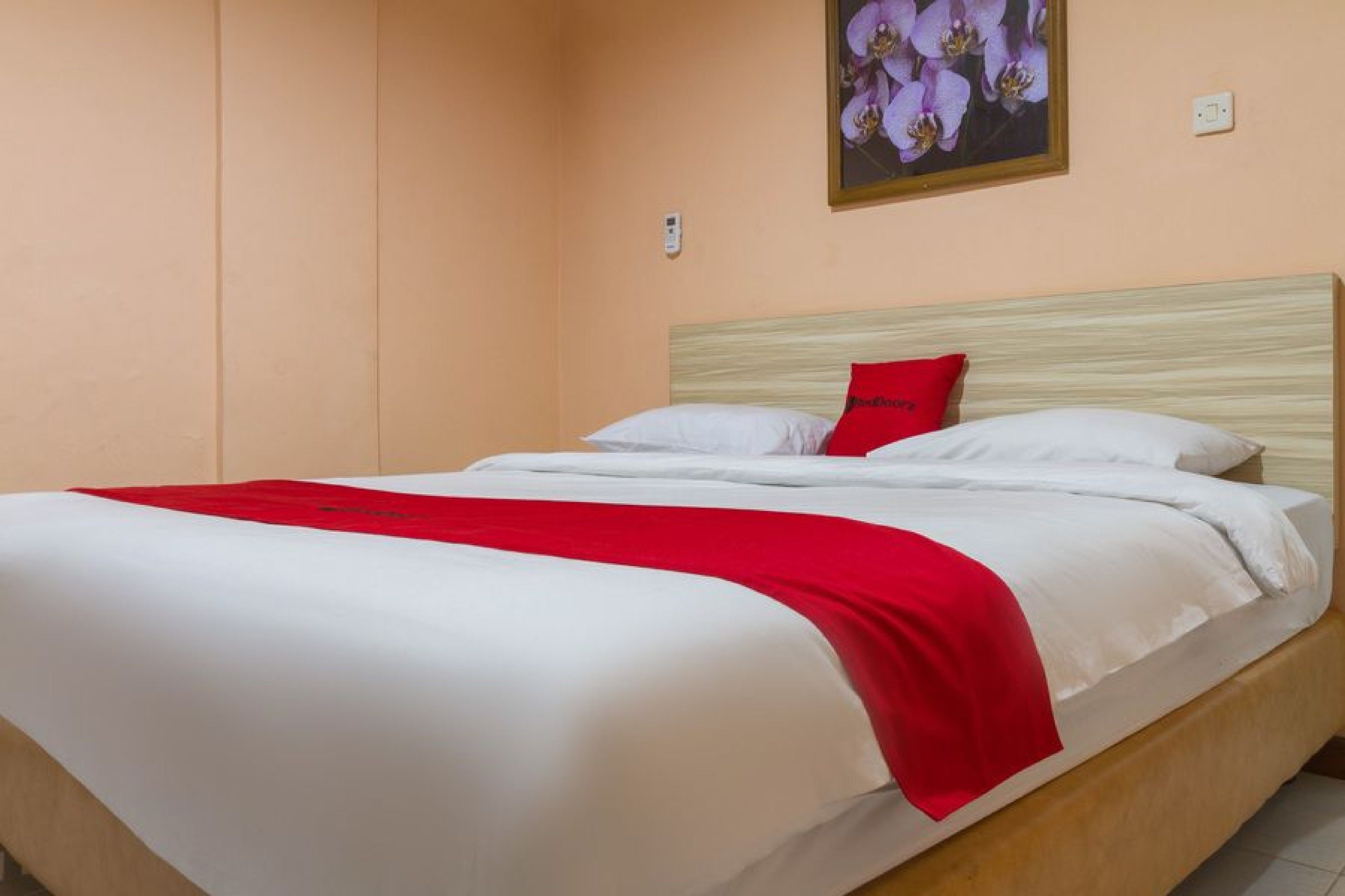 A single bed with a wooden headboard, white bedding, and a red throw blanket.