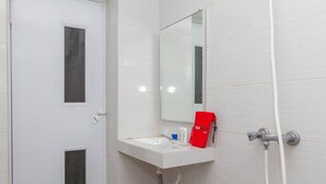 Une salle de bain avec un lavabo blanc, un miroir, une serviette rouge et un flexible de douche.