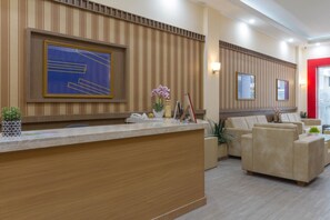 A reception area with a wooden reception desk, beige sofas, and a large abstract painting on the wall.