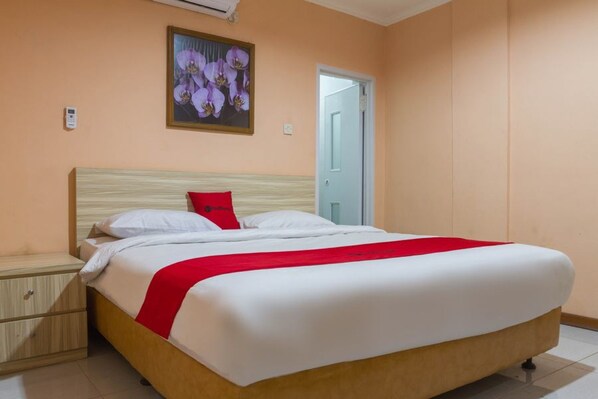 A neatly made bed with white and red bedding, a wooden headboard, and a small bedside table with drawers.