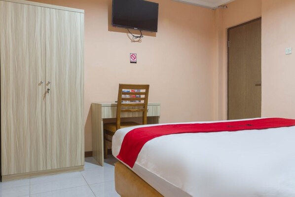 A bedroom with a bed, a wardrobe, a desk with a chair, a television, and a door. - RedDoorz near Istana Plaza 2 (Bandung)