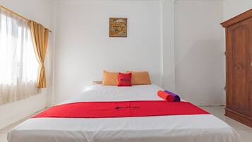Una habitación de hotel con una cama, una colcha roja, un armario de madera y un cuadro en la pared.