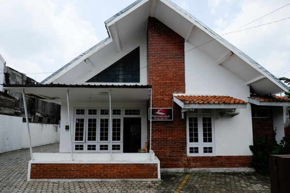A two-story building with a white facade and red brick accents, featuring a covered porch and a visible sign. - RedDoorz near Moro Mall Purwokerto (Purwokerto)
