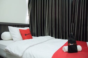 A hotel room with a neatly made bed, a red pillow, a black bag, and a white towel. - RedDoorz near GOR Satria Purwokerto (Purwokerto)
