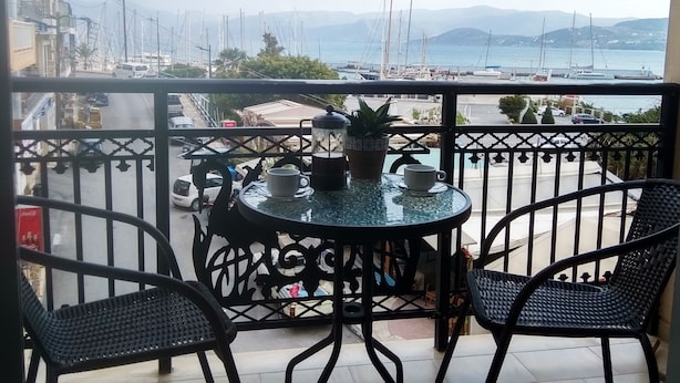 Un balcó amb taula i cadires, amb vista a una marina plena de vaixells i un paisatge de muntanya.