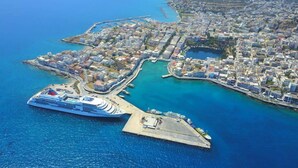 Vista aèria d'una ciutat costanera amb un vaixell de creuer amarrat a un port, envoltat d'edificis residencials i una marina.