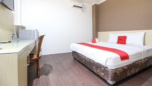 A hotel room with a bed, a desk, a chair, a TV, and an air conditioning unit. - RedDoorz near Stadion Manahan Solo (Surakarta)