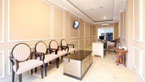 A hotel lobby with a reception desk, a seating area with striped chairs, and a television mounted on the wall. - RedDoorz near Stadion Manahan Solo (Surakarta)