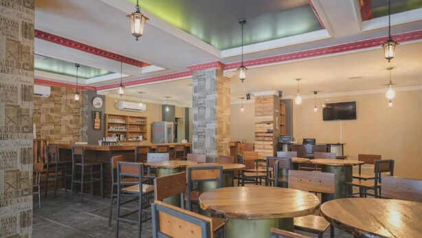 Un restaurant avec des tables et des chaises en bois rondes, un coin bar et un mur décoré d’affiches de style rétro.