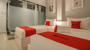 Une chambre d’hôtel avec deux lits, chacun agrémenté de draps rouges et blancs, et une douche en verre.