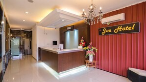 Un hall d’accueil d’hôtel au design moderne, comprenant un comptoir d’accueil, un lustre et une enseigne indiquant « Joe Hotel ».