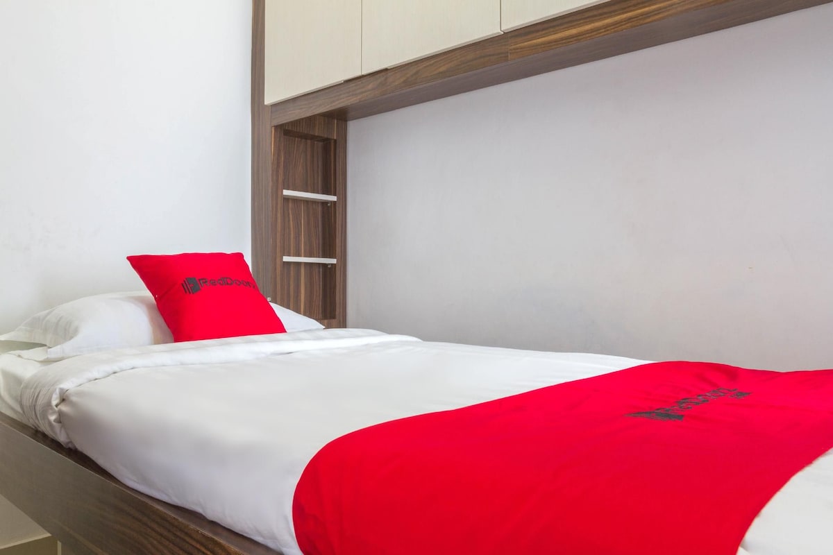 Un lit simple avec un matelas blanc, un oreiller rouge et une couverture rouge.