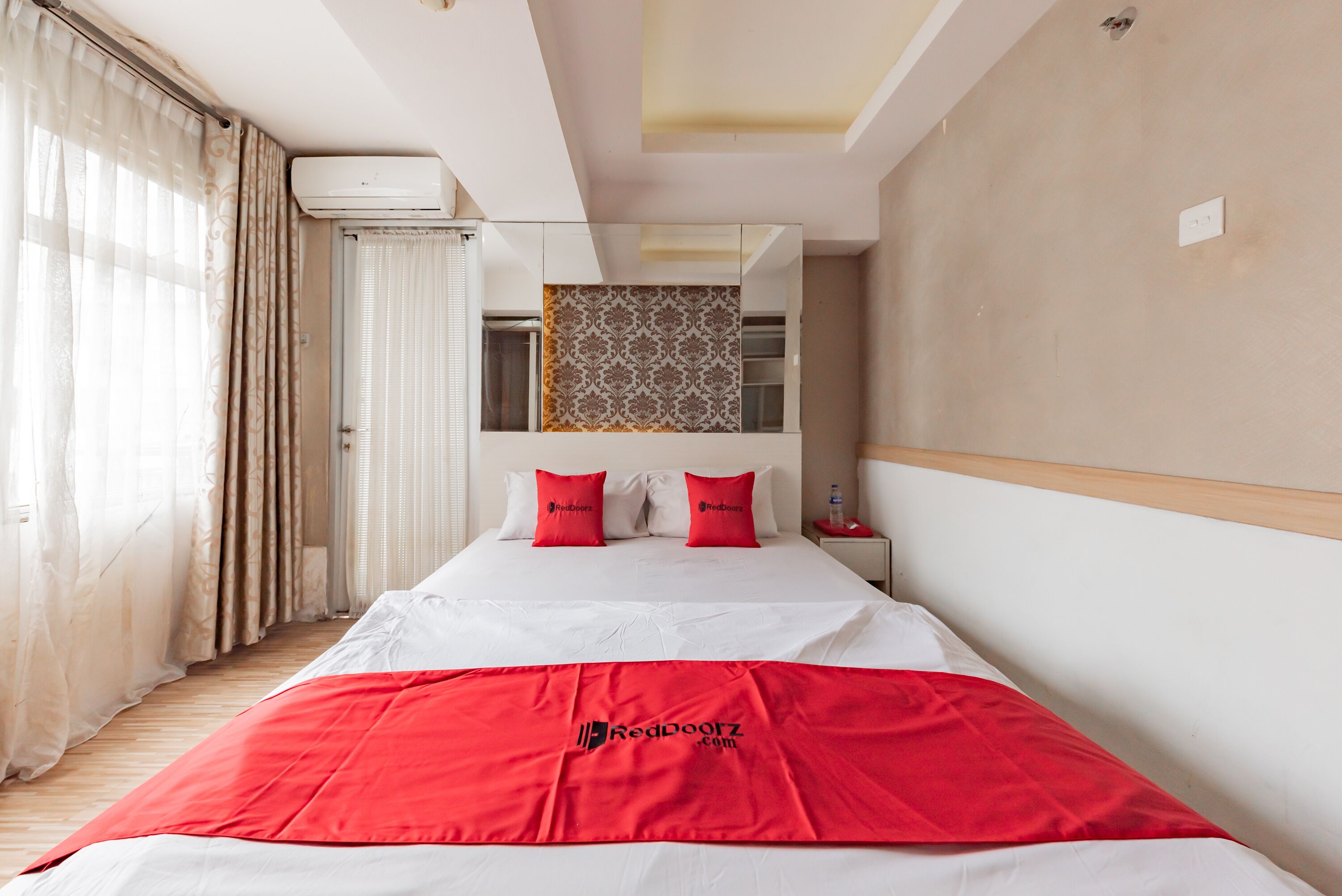 A hotel room with a large bed, a red blanket, and a patterned wall hanging.