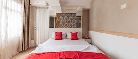 A hotel room with a large bed, a red blanket, and a patterned wall hanging.