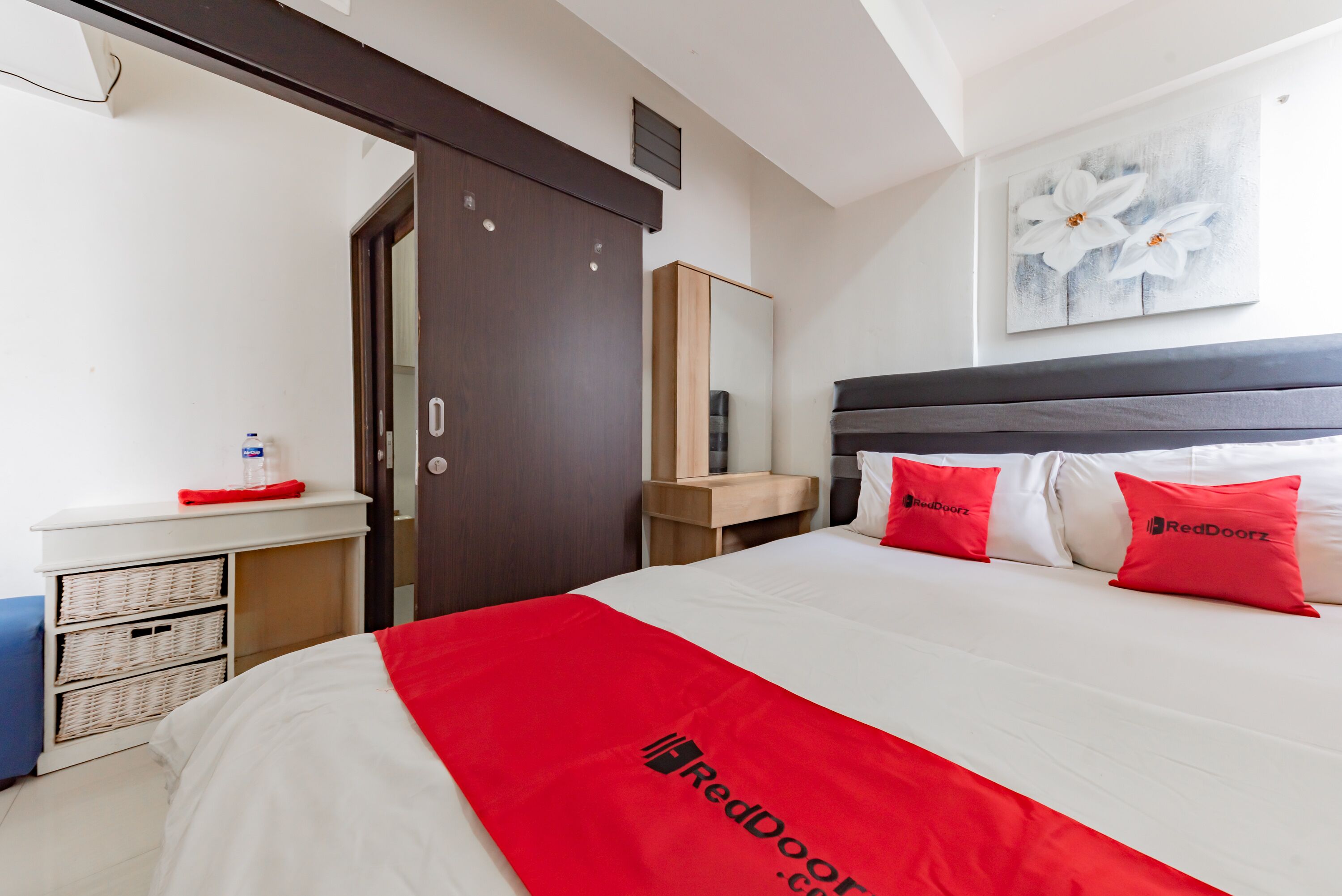 A hotel room with a bed, a wardrobe, a bedside table, and a wall-mounted artwork.