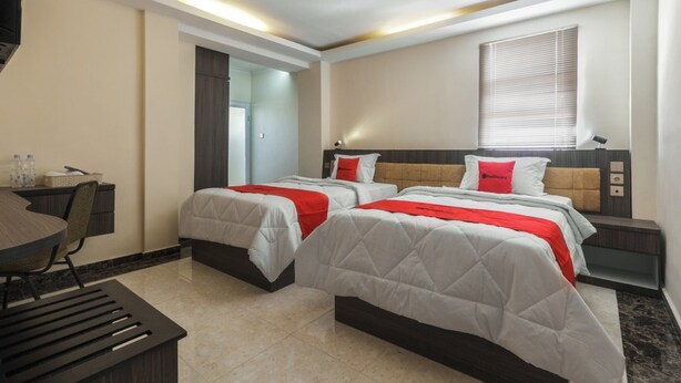 A hotel room with two beds, a desk, and a TV. - RedDoorz Plus @ Boulevard Panakkukang (Makassar)