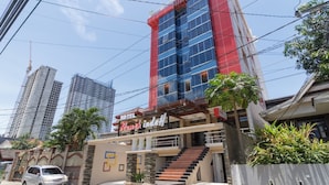 A hotel with a red and blue facade, a staircase leading to the entrance, and a car parked in front. - RedDoorz Plus @ Boulevard Panakkukang (Makassar)